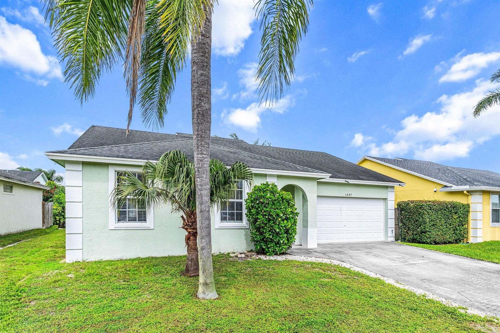 A light green single-story house with a white garage and a palm tree in front — 1087 Salmon Isle, FL 33413, FL