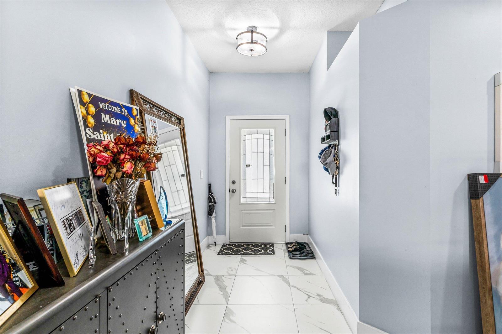 A bright entryway features white marble-look tile flooring, light blue walls, and a front door — 1087 Salmon Isle, FL 33413, FL