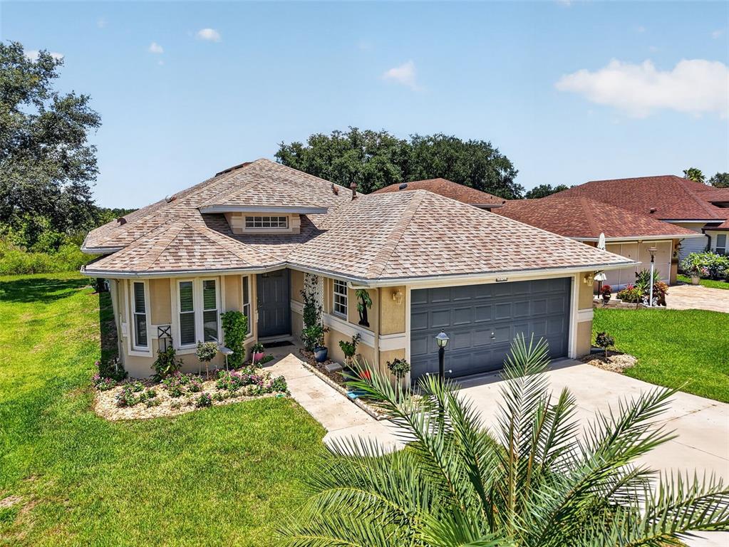 A single-story house with a gray garage, tan stucco walls, and a shingled roof — 21725 KING RICHARDS WAY, LEESBURG, FL