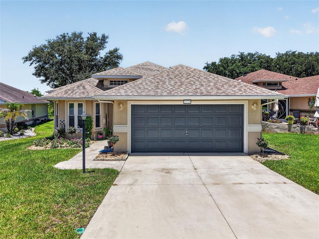 A single-story house with a gray garage door, beige stucco walls, and a shingled roof — 21725 KING RICHARDS WAY, LEESBURG, FL
