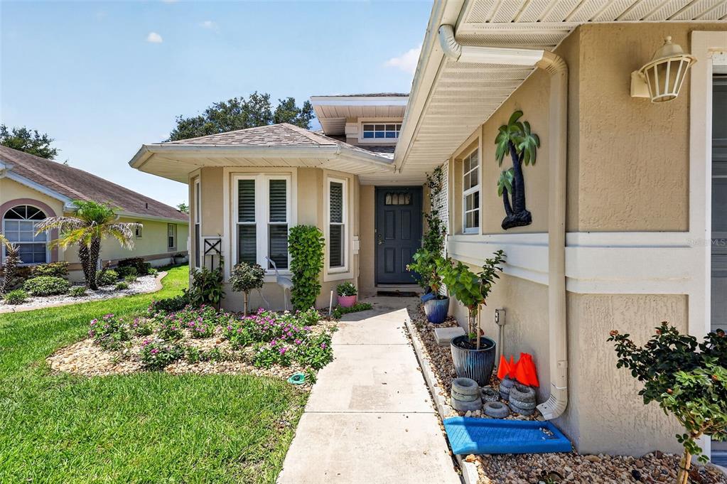 A concrete walkway leads to the front entrance of a tan house with a dark door — 21725 KING RICHARDS WAY, LEESBURG, FL