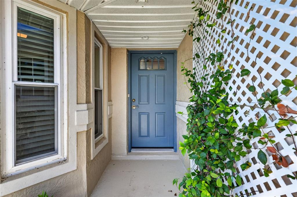 A blue front door is situated in a covered entryway next to a white trellis — 21725 KING RICHARDS WAY, LEESBURG, FL