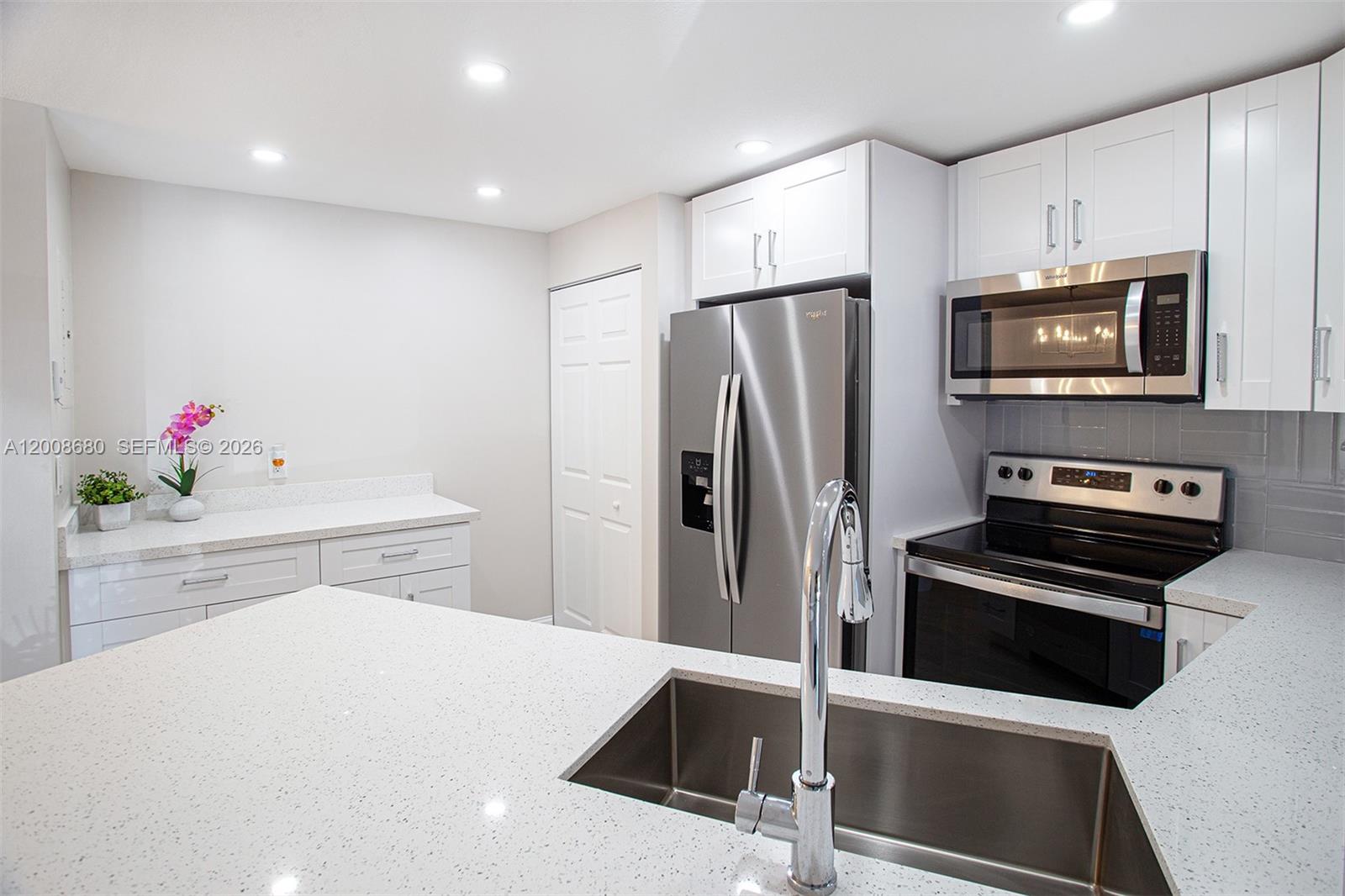 A modern kitchen features white cabinets, stainless steel appliances, and a quartz-topped island with sink — 7527 S Oriole Blvd # 101, Delray Beach FL 33446, DELRAY BEACH, FL