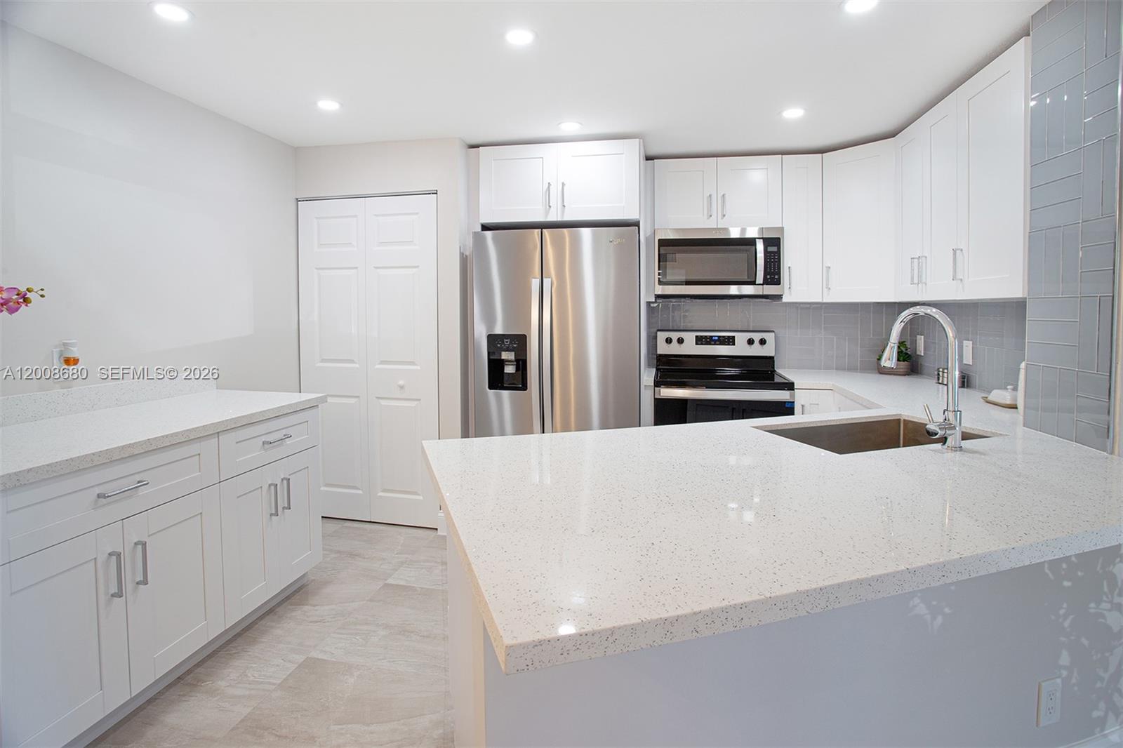 A modern kitchen features white cabinetry, stainless steel appliances, and light-colored quartz countertops — 7527 S Oriole Blvd # 101, Delray Beach FL 33446, DELRAY BEACH, FL
