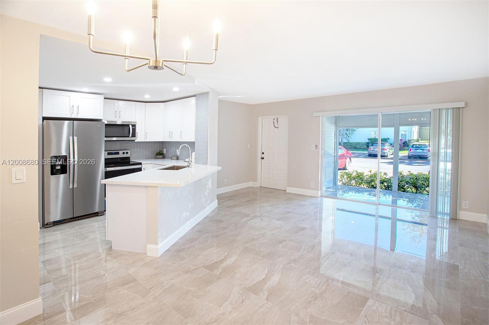A kitchen with white cabinets and stainless steel appliances opens to a tiled living area — 7527 S Oriole Blvd # 101, Delray Beach FL 33446, DELRAY BEACH, FL