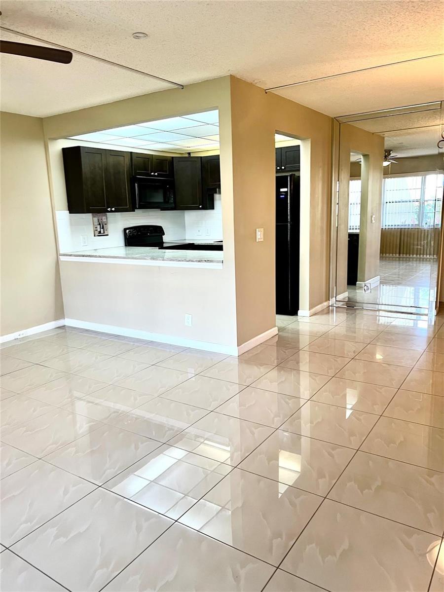 A kitchen with dark cabinets and a breakfast bar opens into a tiled living area — 517 Mansfield M # 517, Boca Raton FL 33434, BOCA RATON, FL