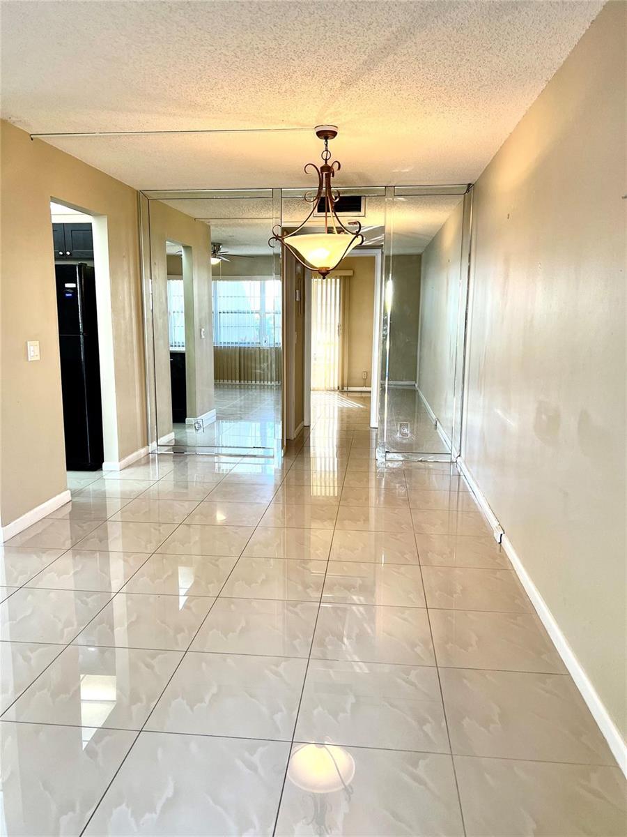 A dining area with large beige floor tiles, mirrored walls, and a hanging light fixture — 517 Mansfield M # 517, Boca Raton FL 33434, BOCA RATON, FL