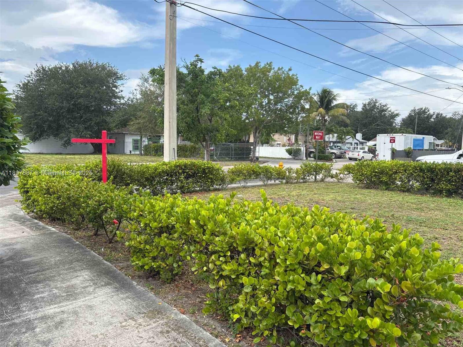 A red real estate sign stands in a grassy lot bordered by a green hedge — 9150 NW 22nd Ave, Miami FL 33147, MIAMI, FL