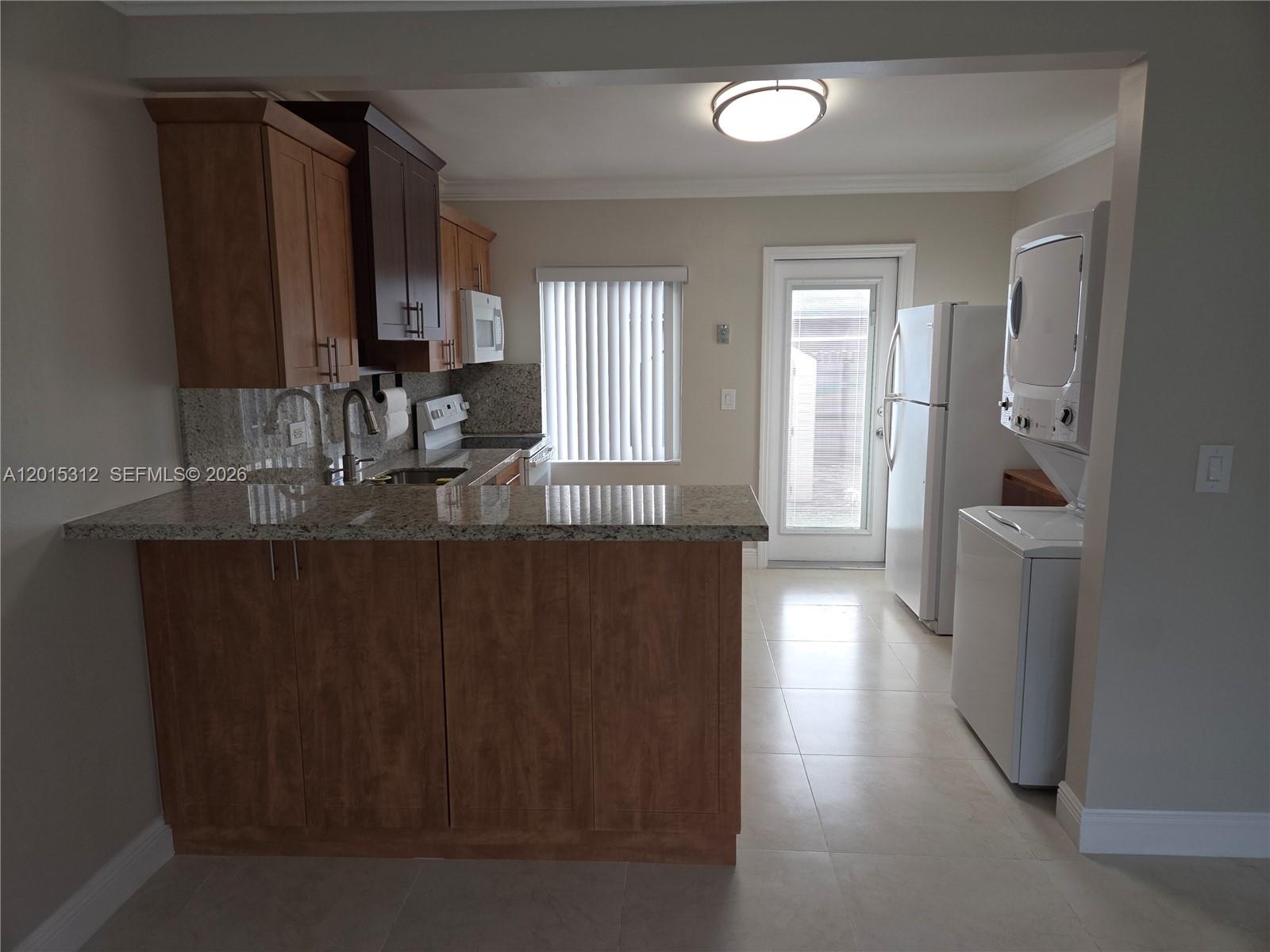 A kitchen features wood cabinets, granite countertops, a white refrigerator, and a stacked laundry unit — 1680 E 5th Ave # 1690, Hialeah FL 33010, HIALEAH, FL