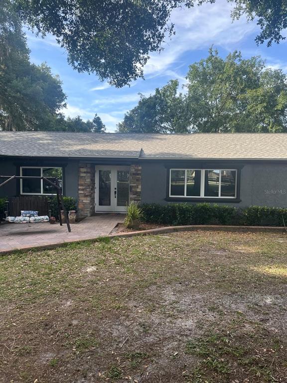 A single-story house with dark gray stucco, stone accents, a paved patio, and a swing — 2700 SE 157TH LANE ROAD, SUMMERFIELD, FL