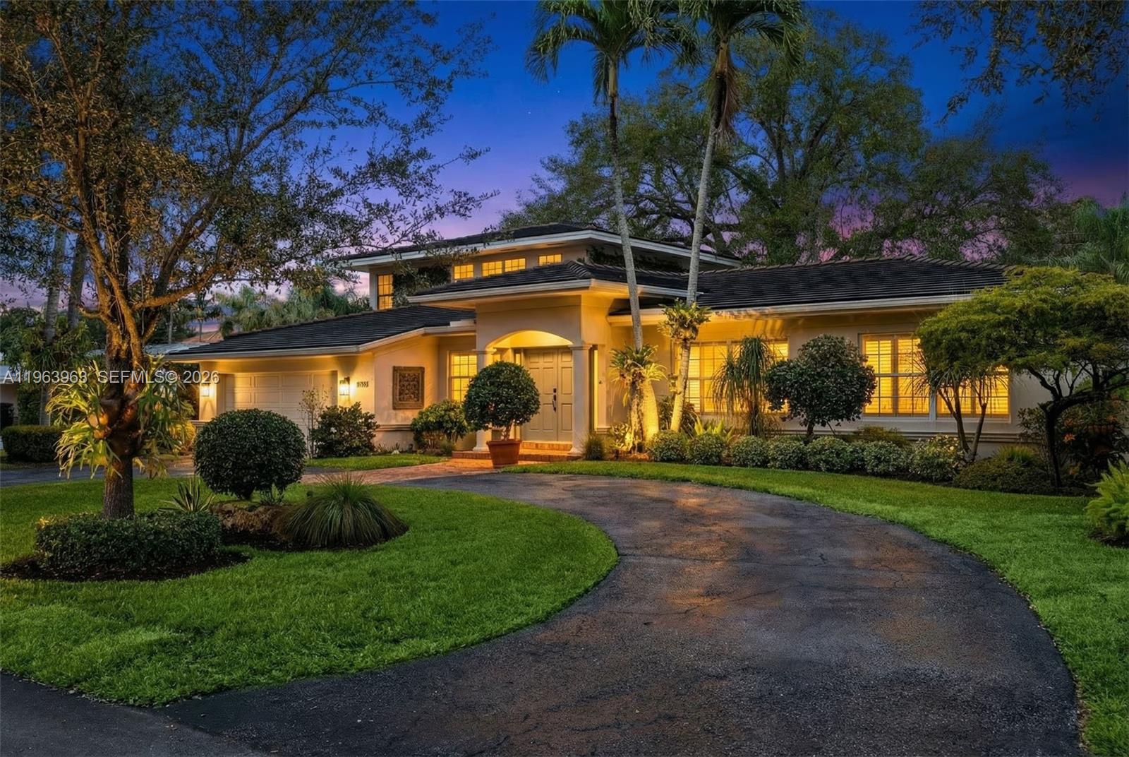 A two-story house with a curved driveway, manicured lawn, and palm trees at dusk — 1255 Algardi Ave, Coral Gables FL 33146, CORAL GABLES, FL