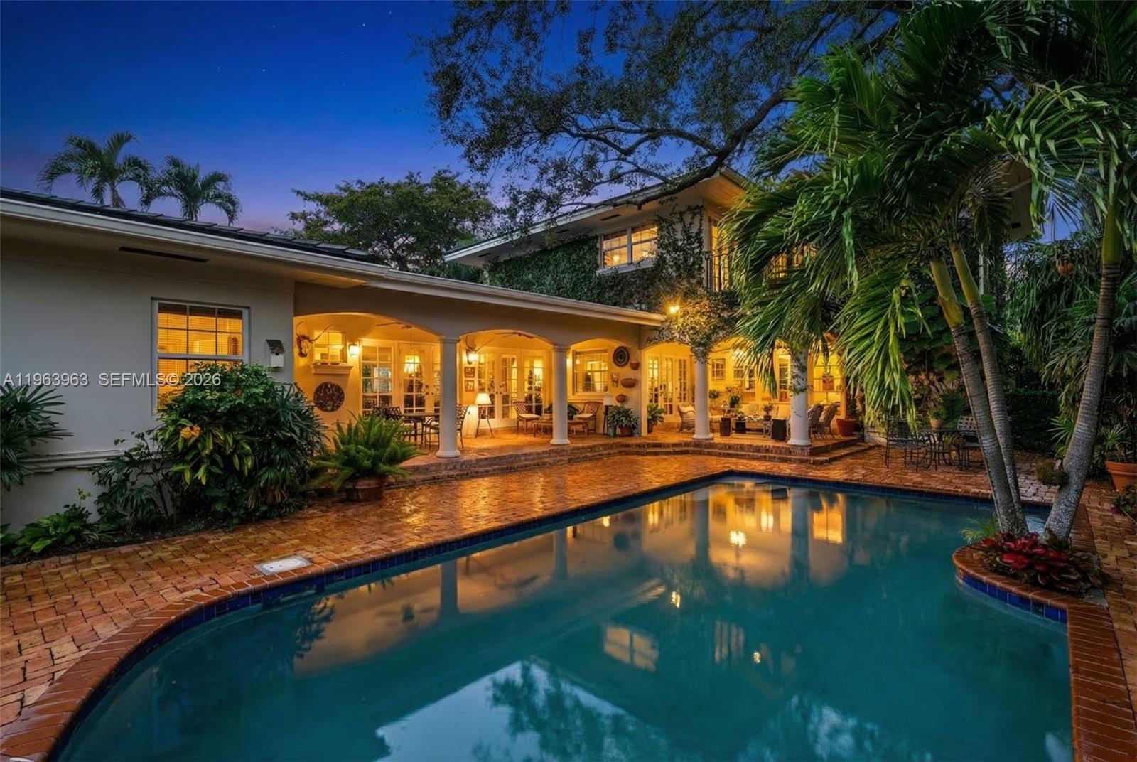 A two-story house with a covered patio overlooks a swimming pool at dusk — 1255 Algardi Ave, Coral Gables FL 33146, CORAL GABLES, FL