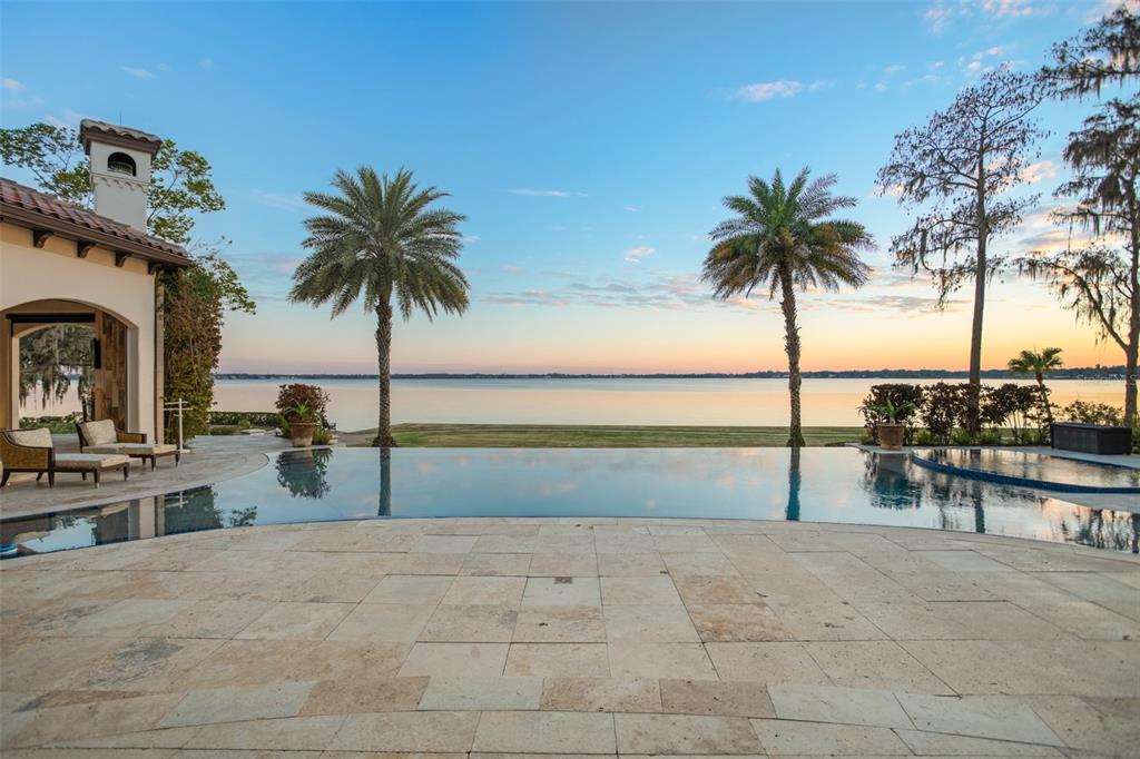 An infinity pool overlooks a large lake from a stone patio with two palm trees — 11900 LAKE BUTLER BOULEVARD, WINDERMERE, FL