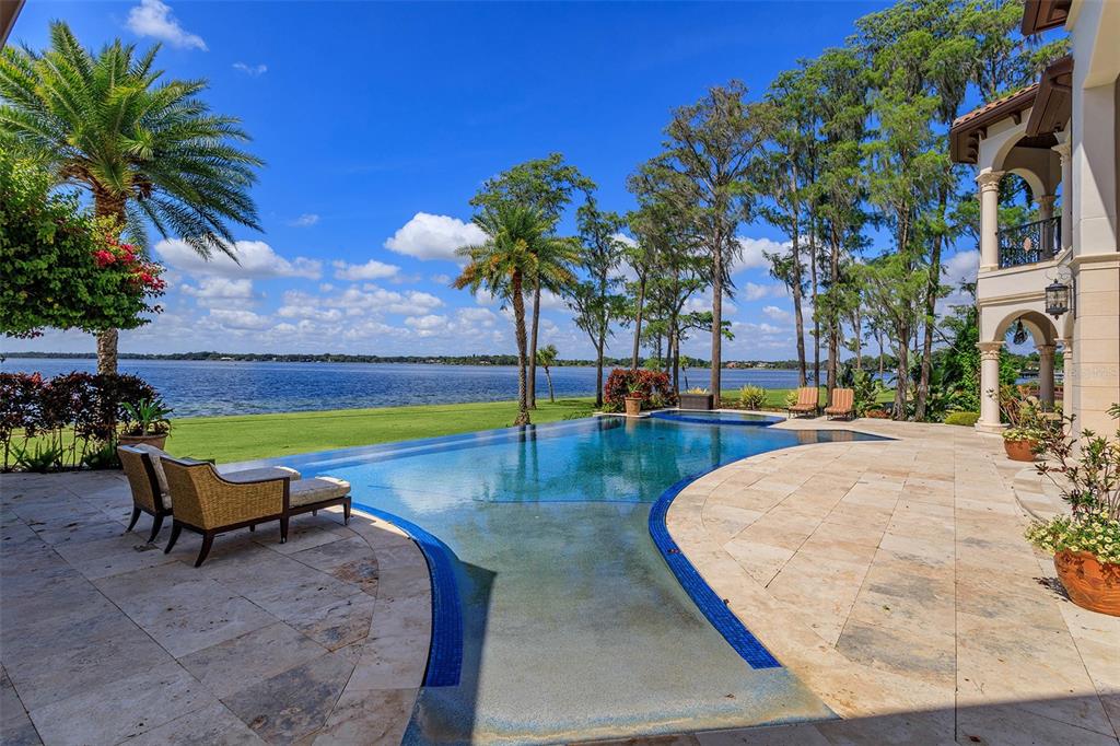 A patio with a curved infinity pool overlooks a large lake and grassy lawn — 11900 LAKE BUTLER BOULEVARD, WINDERMERE, FL