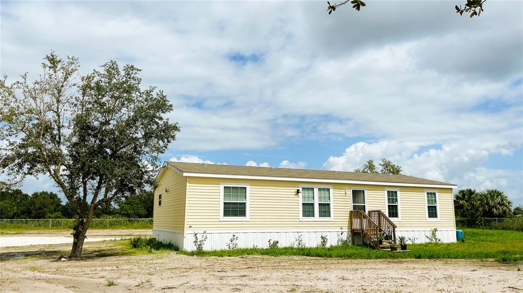 A yellow single-wide manufactured home sits on a dirt lot under a cloudy sky — 16161 NW 276TH STREET, OKEECHOBEE, FL