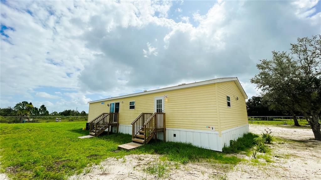 A yellow mobile home with two wooden staircases sits on a grassy lot — 16161 NW 276TH STREET, OKEECHOBEE, FL