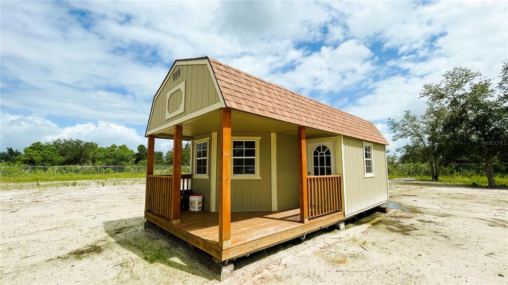 A small, light green wooden shed with a front porch sits on a sandy lot — 16161 NW 276TH STREET, OKEECHOBEE, FL