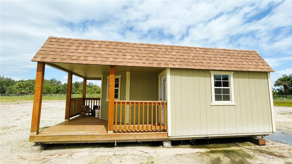 A light green shed with a covered porch, wooden railings, and a brown shingled roof — 16161 NW 276TH STREET, OKEECHOBEE, FL
