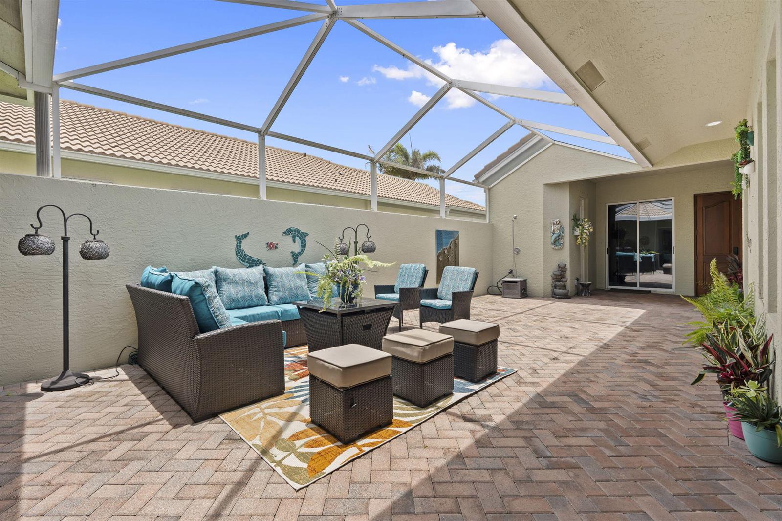 A screened-in patio features a brick paver floor, outdoor furniture, and a light-colored stucco wall — 3320 Caracal Drive, Fort Pierce FL 34949, FORT PIERCE, FL