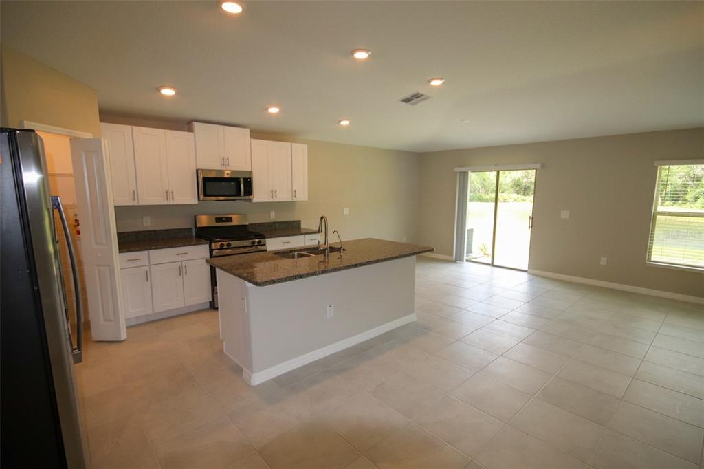 A kitchen with white cabinets, granite countertops, and an island opens to a living area — 10347 ALDER GREEN DRIVE, RIVERVIEW, FL