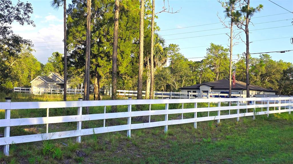 A white split-rail fence encloses a grassy lot with two houses and tall pine trees — 10379 THRASHER AVENUE, WEEKI WACHEE, FL
