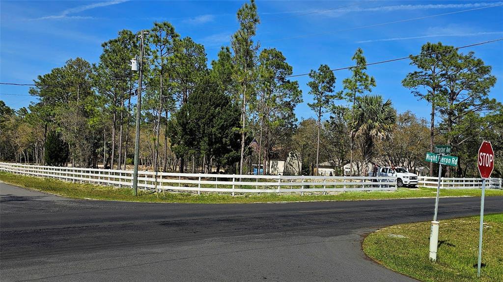 A white fence encloses a wooded lot at the corner of a paved road — 10379 THRASHER AVENUE, WEEKI WACHEE, FL
