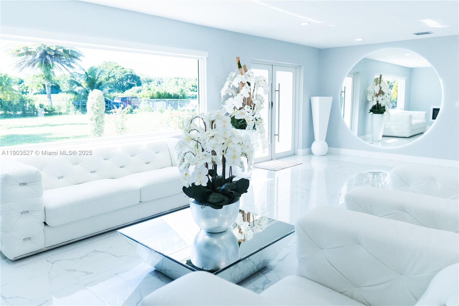 A bright, all-white living room features tufted sofas, a mirrored coffee table, and a large circular mirror — 19245 SW 188th St, Miami FL 33187, MIAMI, FL