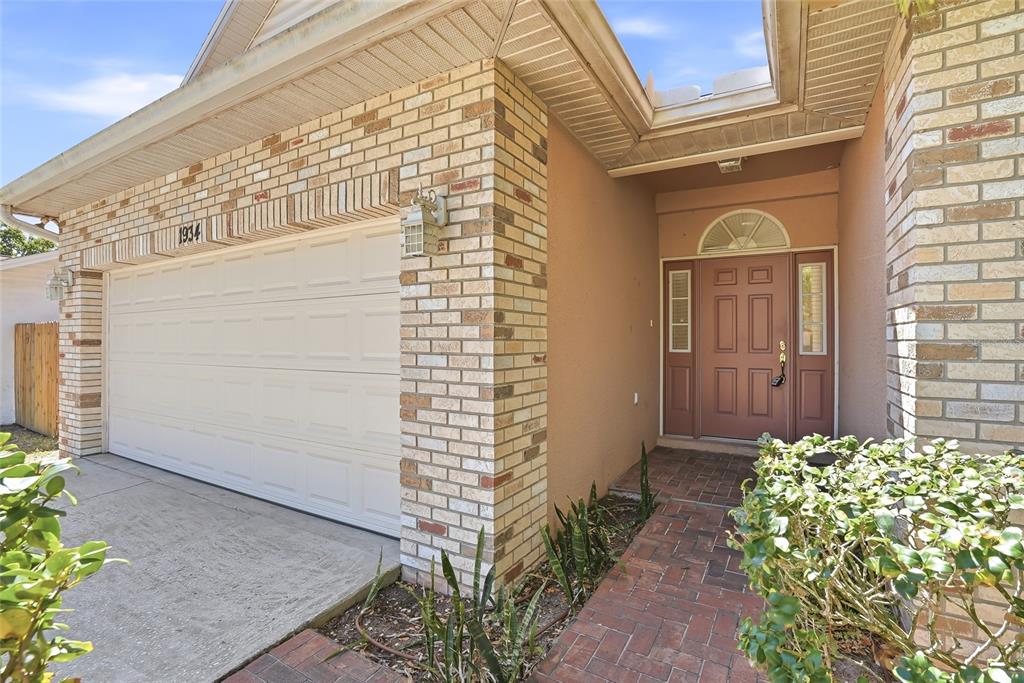 The exterior of a house features a brick-trimmed garage, a brown front door, and landscaping — 1934 OLD SAWMILL ROAD, BRANDON, FL