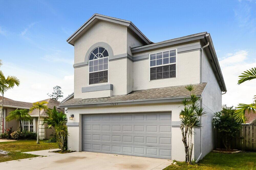 A two-story house with a gray garage door, stucco exterior, and an arched upper window — WELLINGTON, FL