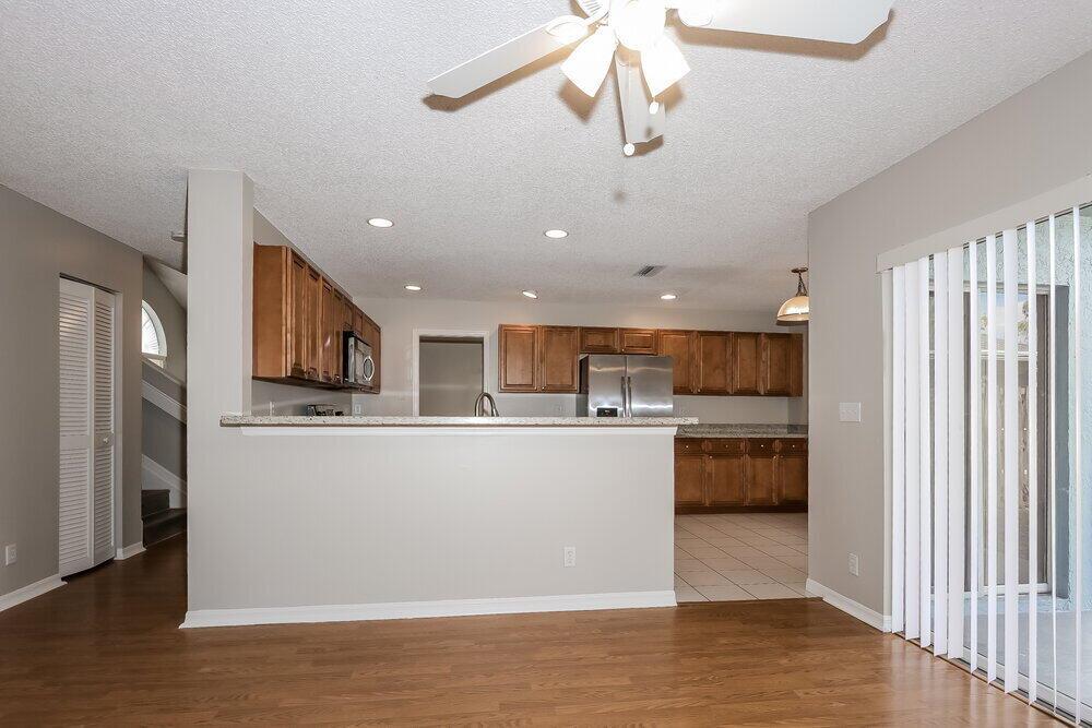 A kitchen with wood cabinets and stainless steel appliances overlooks a living area with flooring — WELLINGTON, FL