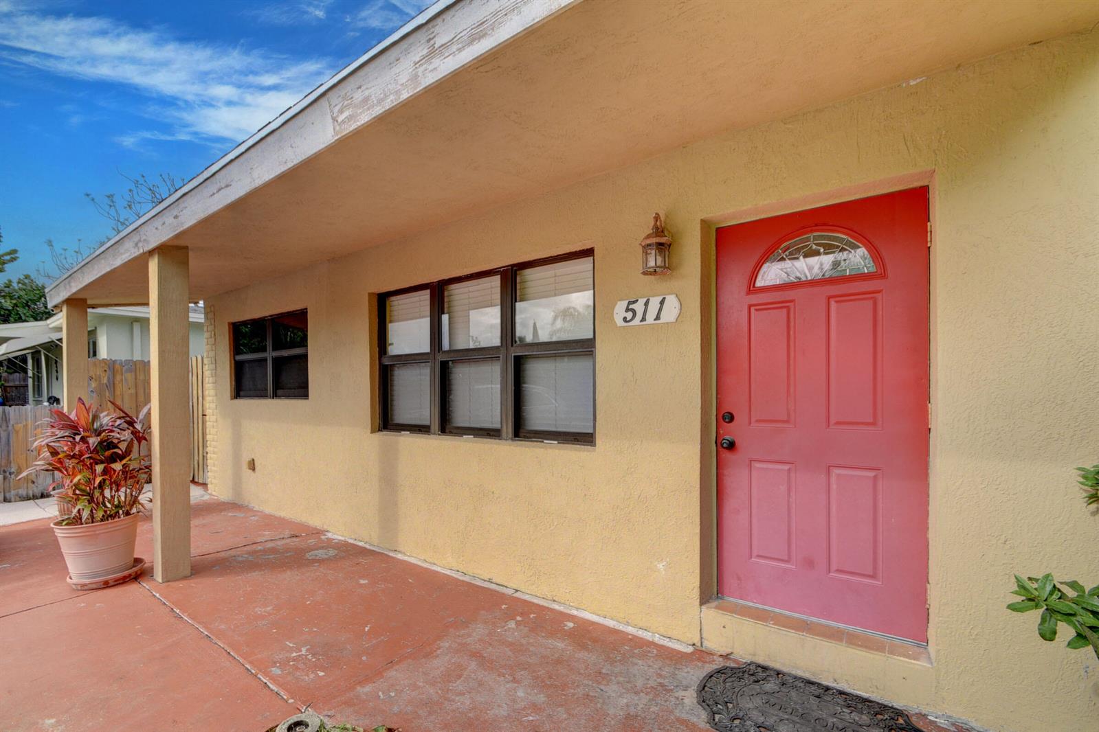 A yellow exterior wall features a red front door, a window, and a covered porch — 511 Minnesota Street, Lantana FL 33462, LANTANA, FL