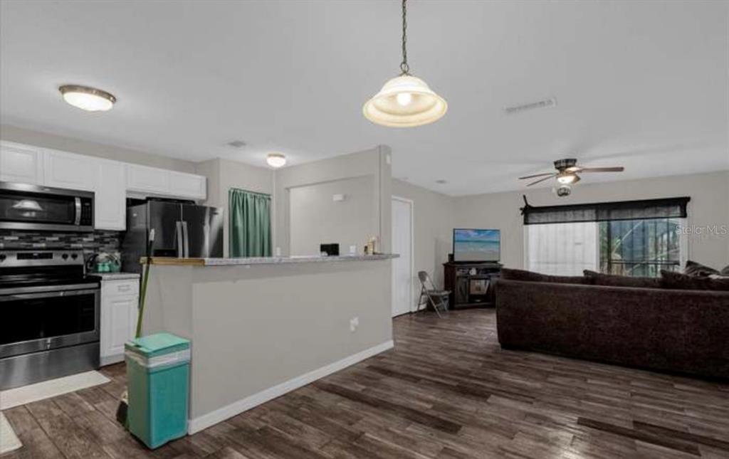 An open-concept kitchen and living area featuring white cabinets, stainless appliances, and dark wood flooring — 1783 FLORES COURT, ORLANDO, FL