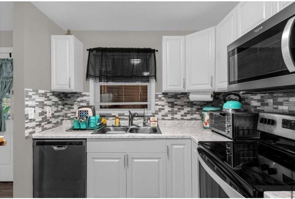 A kitchen features white cabinets, a gray tiled backsplash, a double sink, and stainless appliances — 1783 FLORES COURT, ORLANDO, FL