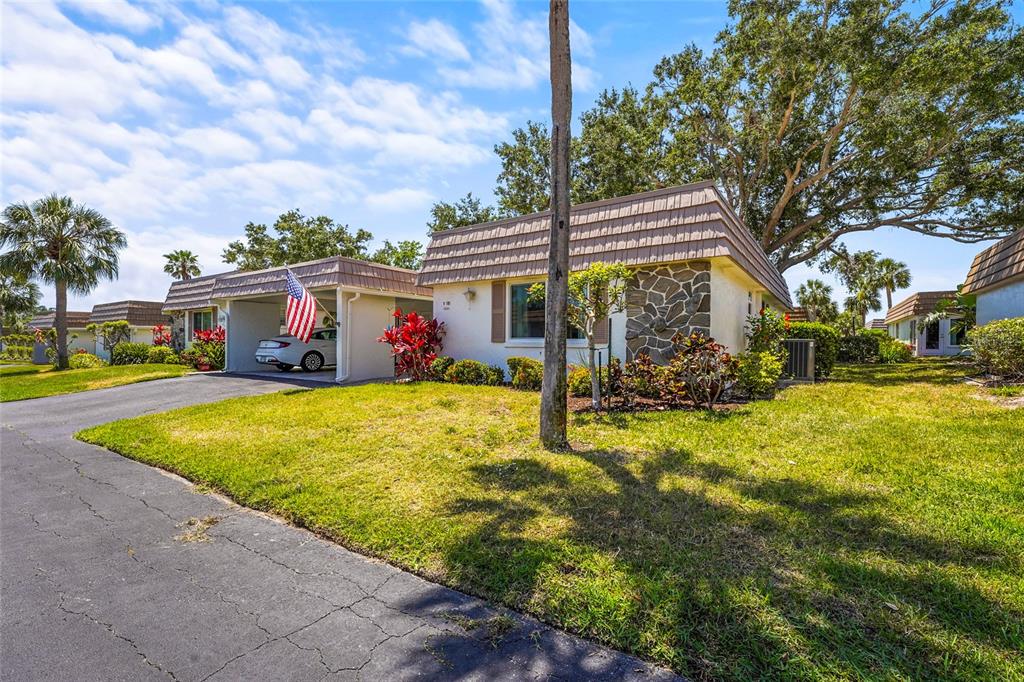 A single-story house with a carport, stone facade, and a large tree in the front yard — 2531 RIVERBLUFF PARKWAY UNIT V181, SARASOTA, FL