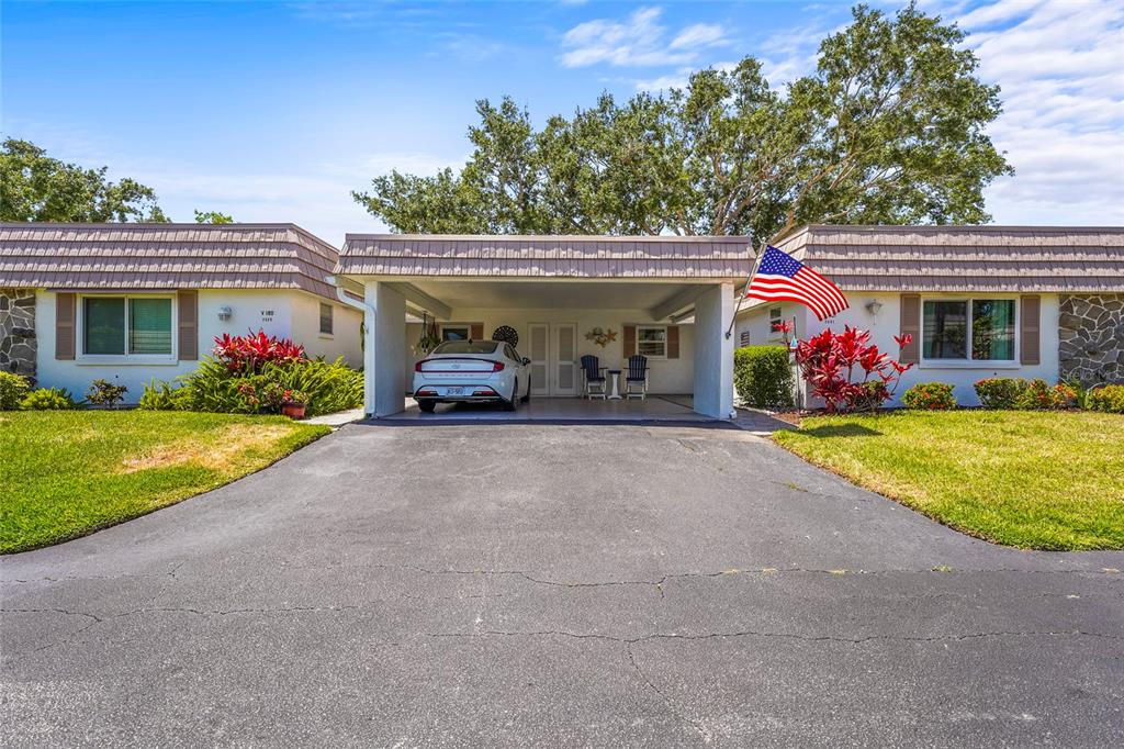 A single-story house features a central carport, a paved driveway, and an American flag — 2531 RIVERBLUFF PARKWAY UNIT V181, SARASOTA, FL