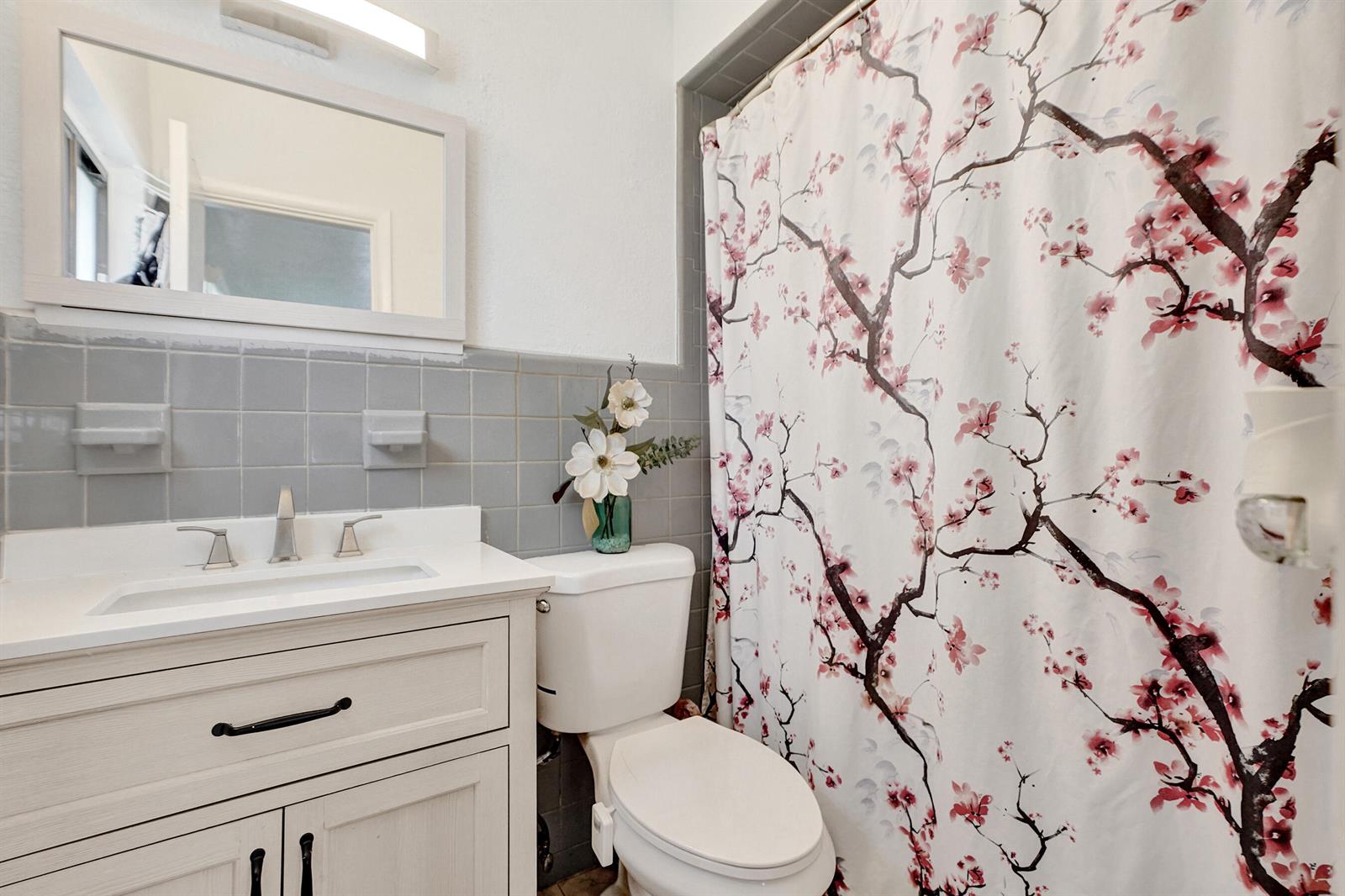 A bathroom features a white vanity, gray tiled walls, a toilet, and a floral shower curtain — 1070 NW 149th Street, Miami FL 33168, MIAMI, FL