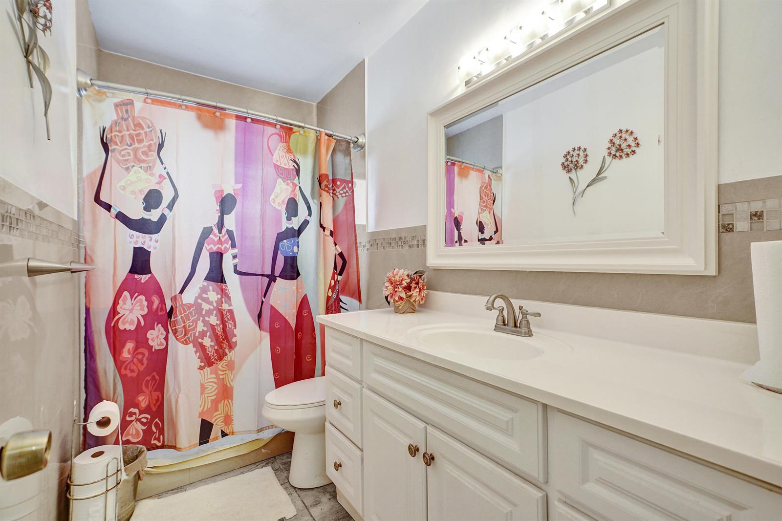 A bathroom features a white vanity, a large mirror, and a colorful patterned shower curtain — 1070 NW 149th Street, Miami FL 33168, MIAMI, FL