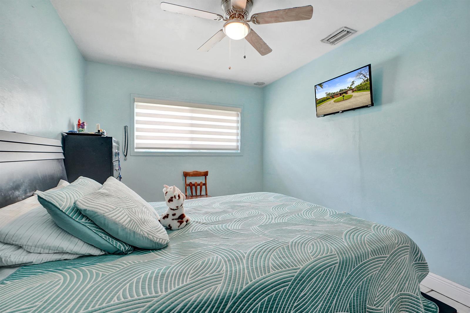 A bedroom with light blue walls, a patterned bedspread, a ceiling fan, and a wall-mounted television — 1070 NW 149th Street, Miami FL 33168, MIAMI, FL