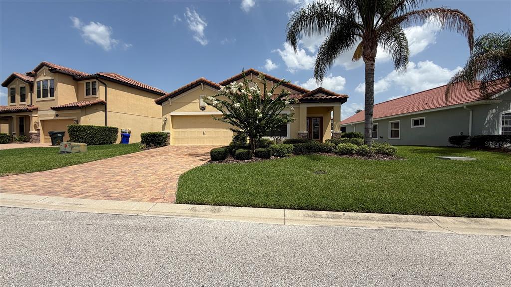 A single-story yellow house with a tiled roof, paver driveway, and a palm tree — 1947 ALTAVISTA CIRCLE, LAKELAND, FL