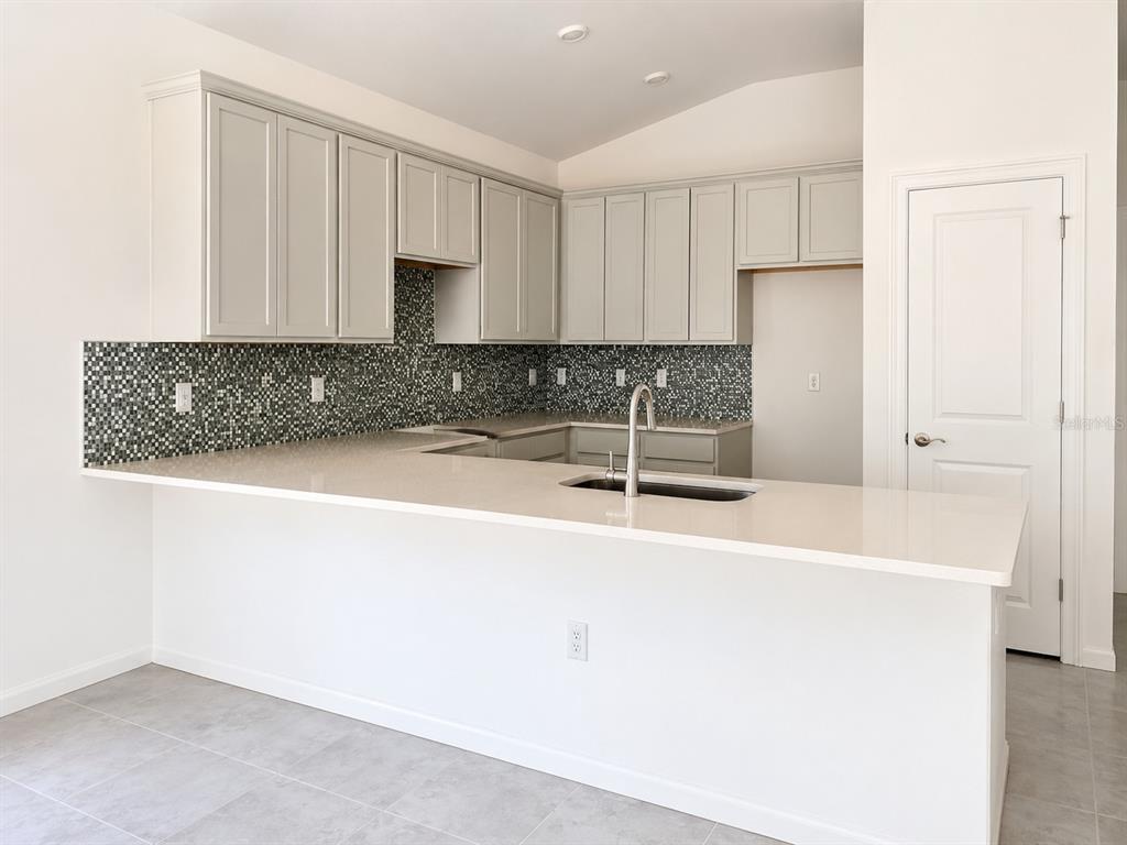 A kitchen features light gray cabinets, a mosaic tile backsplash, and a white countertop island — 434 ALBATROSS ROAD, ROTONDA WEST, FL