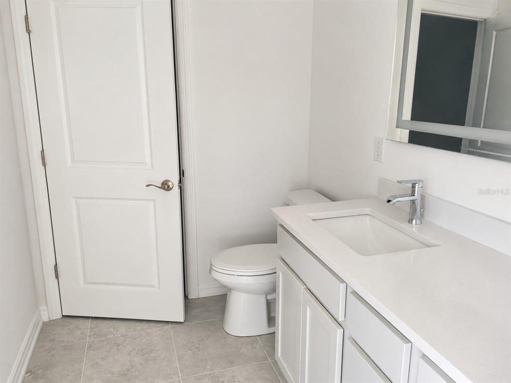 A bathroom features a white vanity with a sink, a toilet, and a closed door — 434 ALBATROSS ROAD, ROTONDA WEST, FL