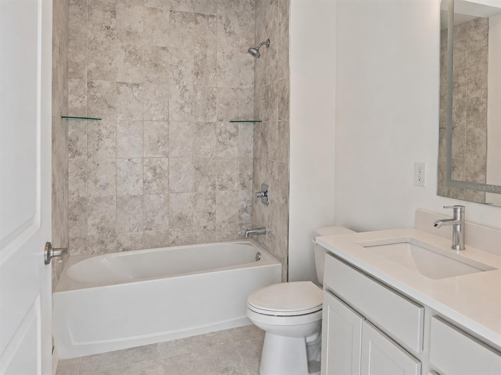 A bathroom features a white vanity, a toilet, and a bathtub with gray tiled walls — 434 ALBATROSS ROAD, ROTONDA WEST, FL