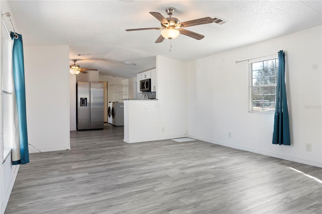 A living room with light gray wood-look flooring, white walls, and an open kitchen area — 6526 JACK STREET, PUNTA GORDA, FL