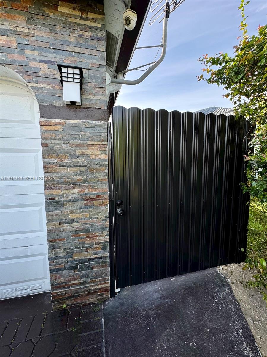 A black corrugated metal gate stands next to a stone-clad wall and a garage — 14234 SW 163rd Ter # 2, Miami FL 33177, MIAMI, FL