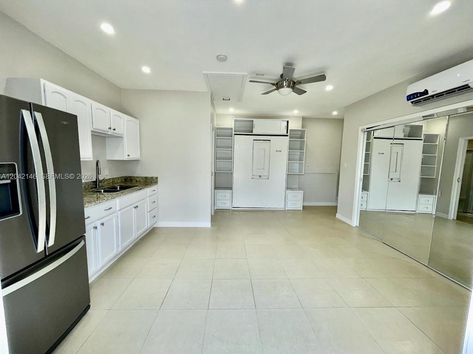 This kitchen and living area features white cabinetry, granite countertops, tile flooring, and a Murphy bed — 14234 SW 163rd Ter # 2, Miami FL 33177, MIAMI, FL