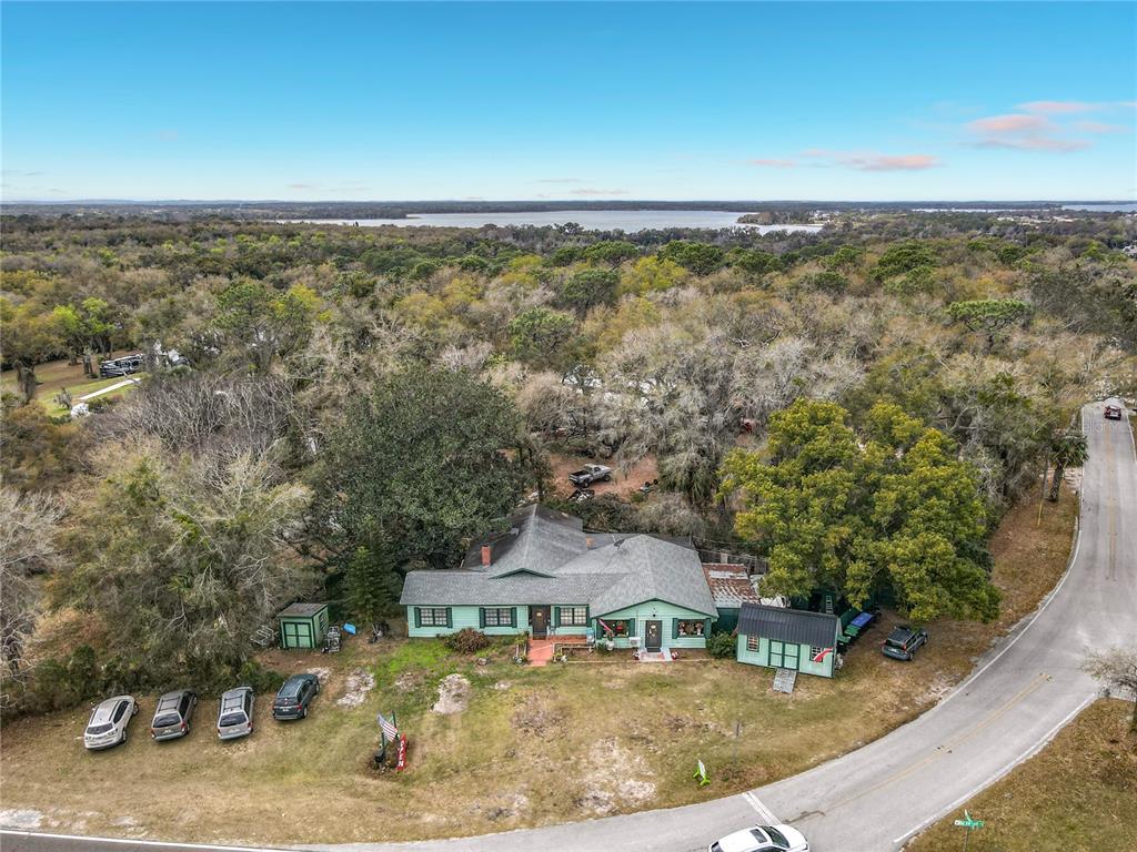 An aerial view shows a light green house with a metal roof near a road — 6942 OLD HIGHWAY 441 S, MOUNT DORA, FL