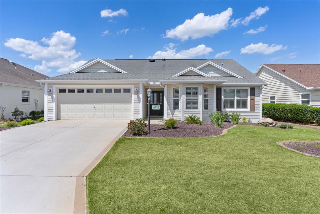 A single-story house with beige siding, a two-car garage, and a front lawn — 1215 WESTMORELAND LOOP, THE VILLAGES, FL