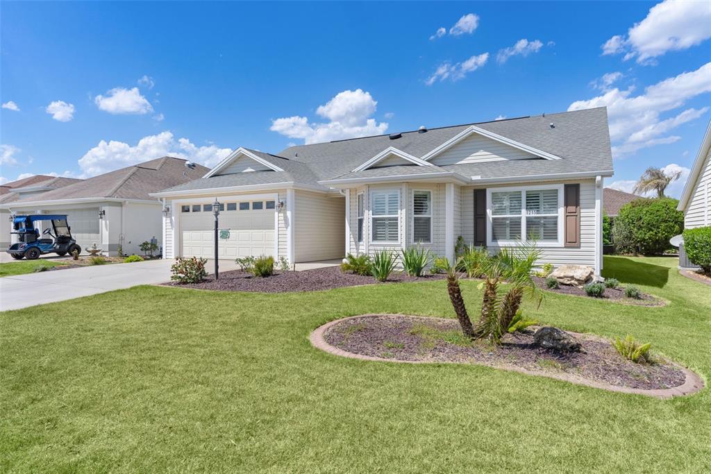 A single-story house with beige siding, a two-car garage, and a landscaped front lawn — 1215 WESTMORELAND LOOP, THE VILLAGES, FL