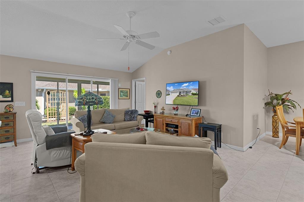 A living room features beige walls, tile flooring, a ceiling fan, and a sliding glass door — 1215 WESTMORELAND LOOP, THE VILLAGES, FL