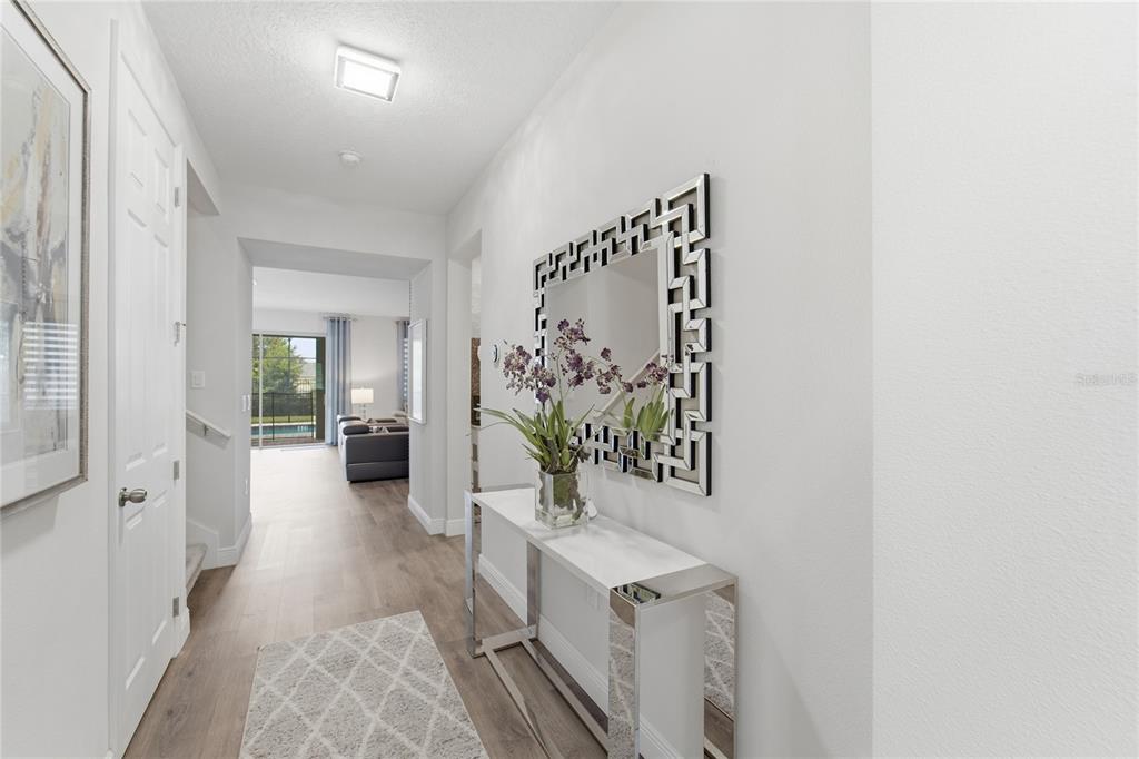 A bright hallway features a mirrored console table, a geometric wall mirror, and light flooring — 9083 SUNSHINE RIDGE LOOP, KISSIMMEE, FL